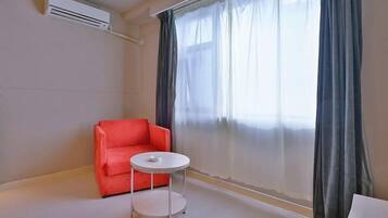 A room with a red sofa, a small round table, and a large window with sheer curtains.
