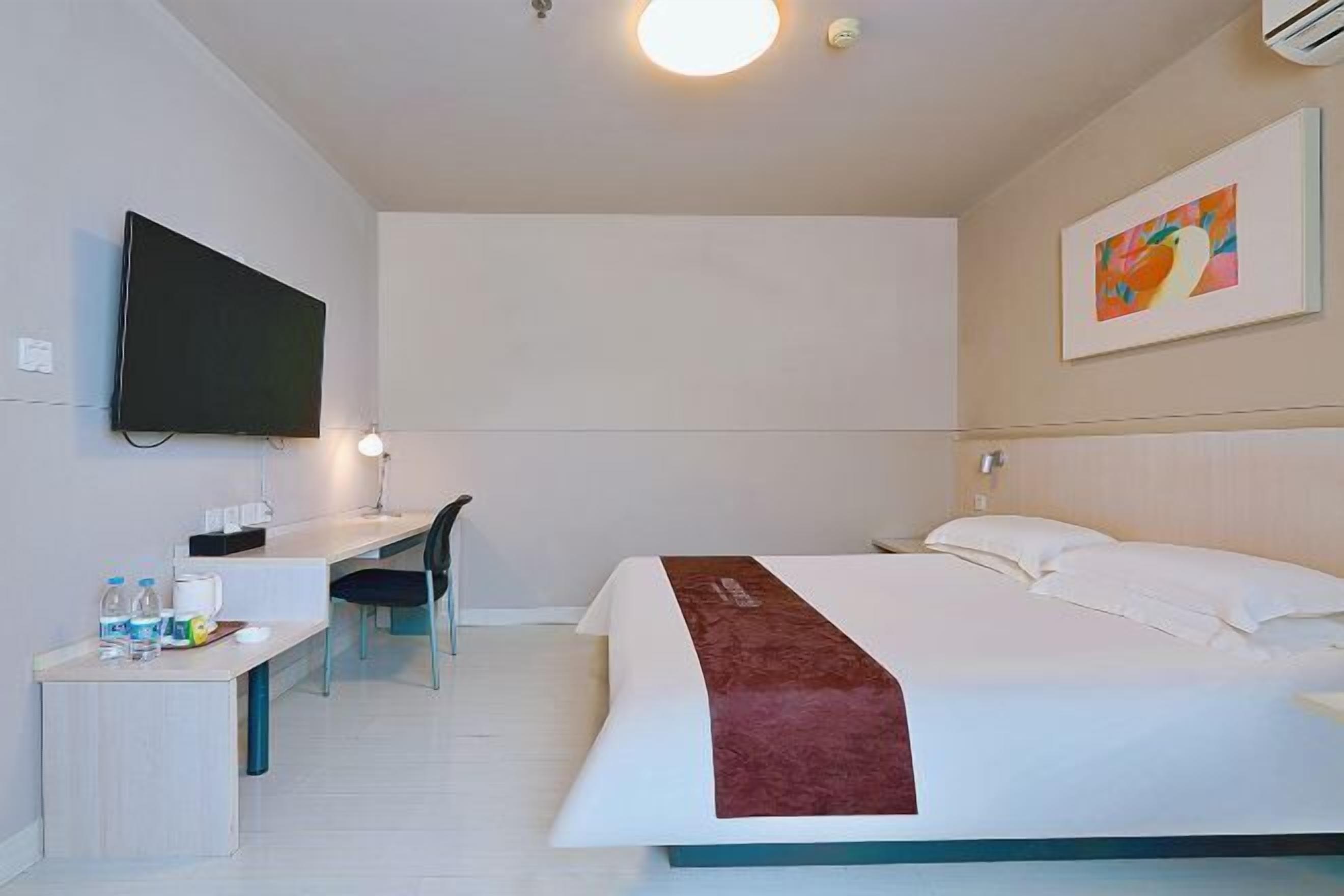 A hotel room with a bed, a desk, a chair, a television, and a painting on the wall.