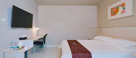 A hotel room with a bed, a desk, a chair, a television, and a painting on the wall.
