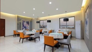 Un espace de restauration moderne avec des tables rondes et des chaises orange, agrémenté de luminaires au plafond et d’œuvres d’art murales.