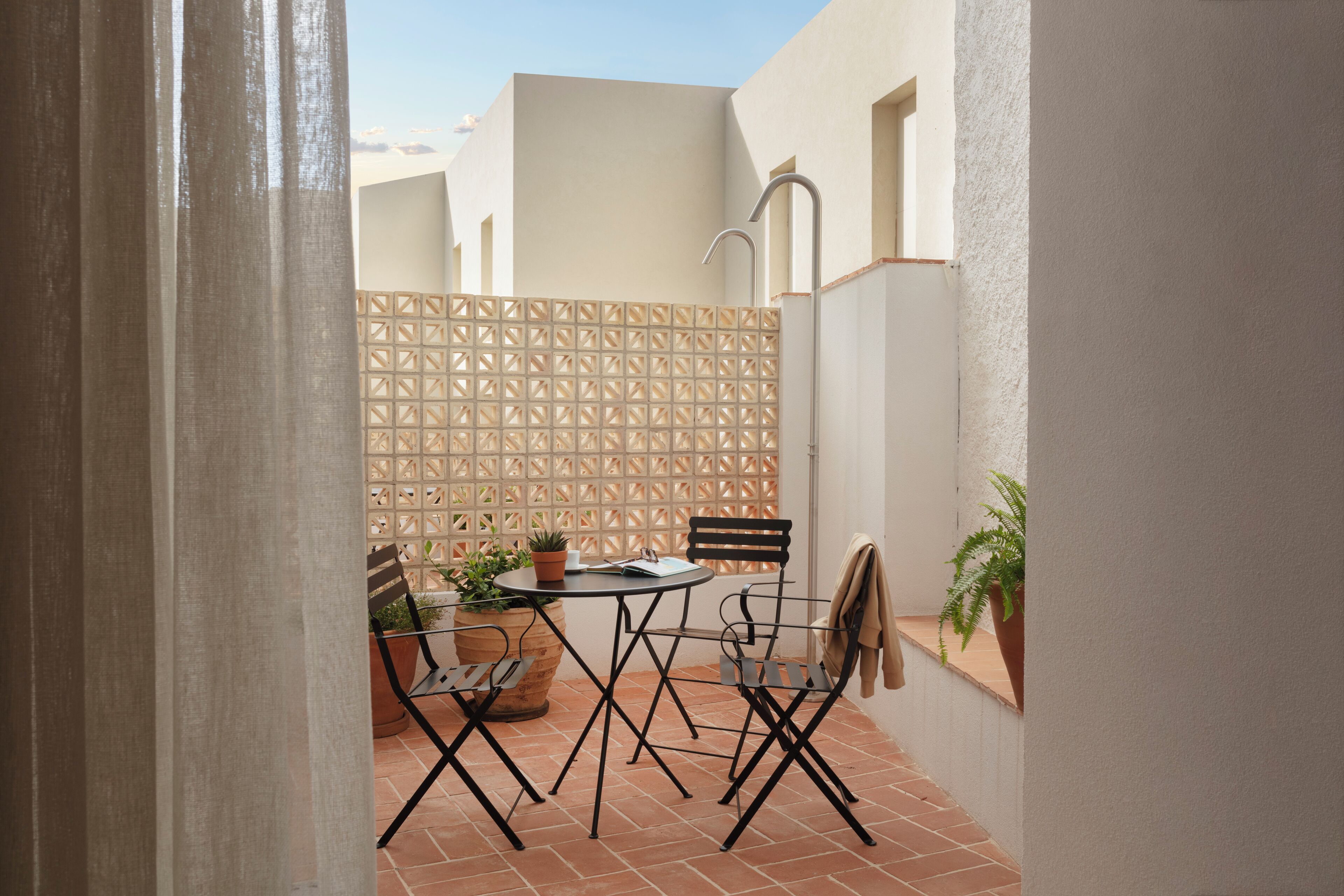 An outdoor patio with a table and chairs, a potted plant, and a decorative wall.