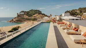 Una piscina con vista a la playa y una estructura que recuerda a un castillo al fondo.