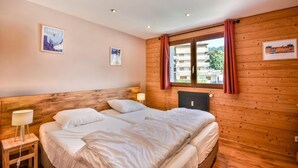 A double bed with white linens, a wooden headboard, a bedside table with a lamp, and a window with curtains.