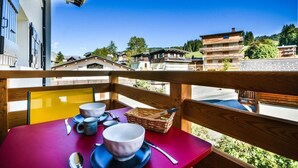 A balcony with a table set for two, overlooking a mountain village with traditional buildings.