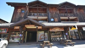 A wooden building with multiple balconies and signs for 'Le Praz du Soleil' and 'L'Eri Getois'. There are picnic tables outside. - 1st floor, balcony, tv, ski locker, 25m², Les Gets (Les Gets)