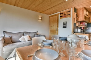 A cozy living area with a sofa, a dining table set with bowls and glasses, and a kitchen with wooden cabinets and appliances.