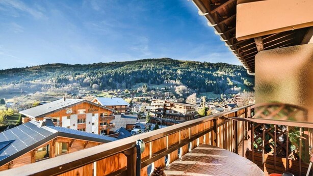 Een houten balkon met uitzicht op een bergstad, inclusief gebouwen en een bebost heuvel.