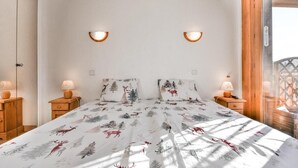 Een slaapkamer met een bed, twee nachtkastjes, twee wandlampen en een raam met houten kader.