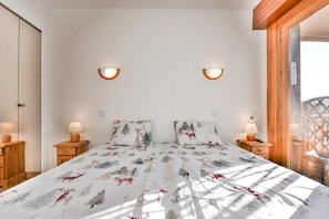 Een slaapkamer met een bed, twee nachtkastjes, twee wandlampen en een raam met houten kader.