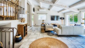 A spacious living room with a large sofa, a coffee table, and a fireplace. There is a staircase with a railing and a wooden cabinet.