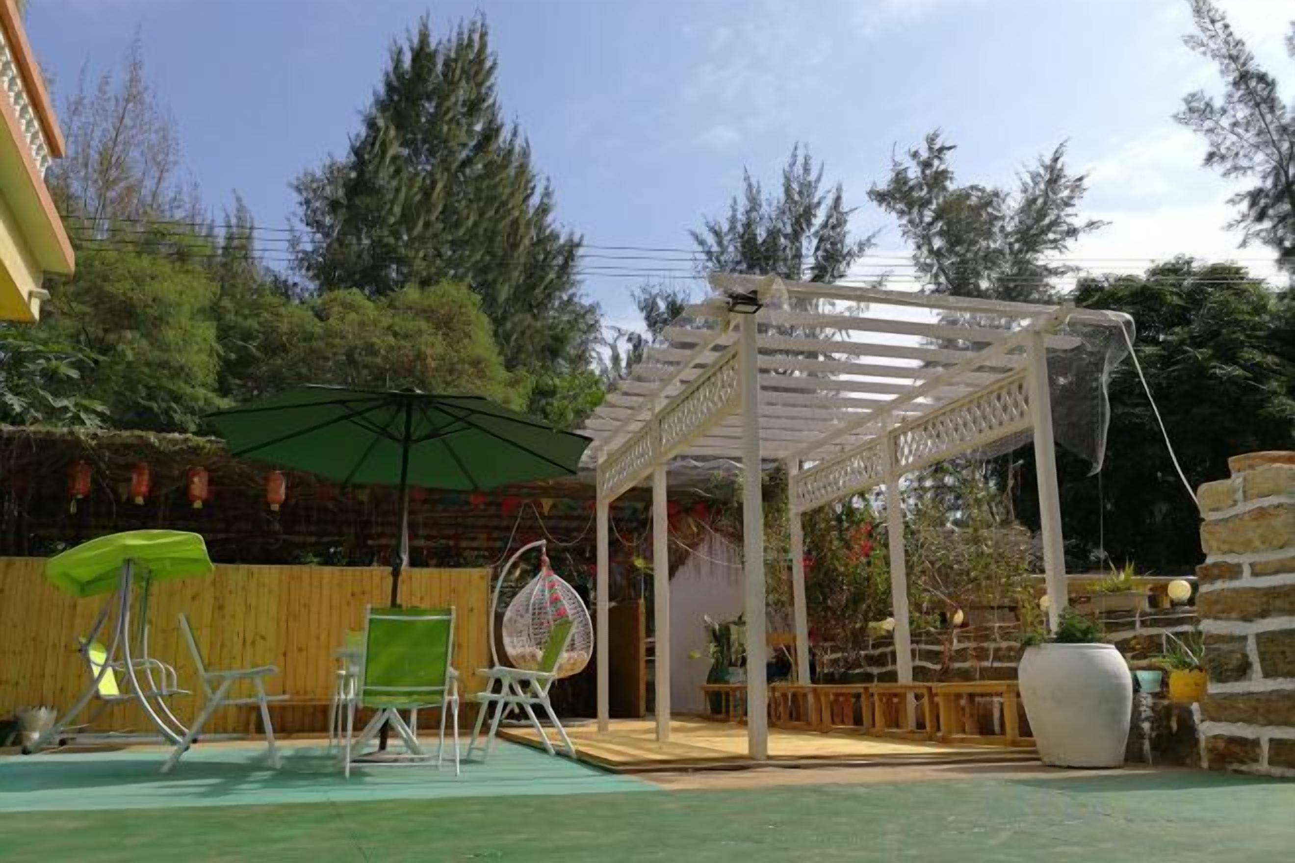 A covered outdoor seating area with a pergola, a hanging chair, and a green umbrella.