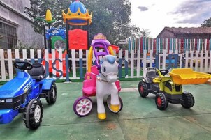 Área externa cercada com diversos equipamentos de recreação infantil, incluindo um trator, um cavalo de brinquedo e um parquinho.