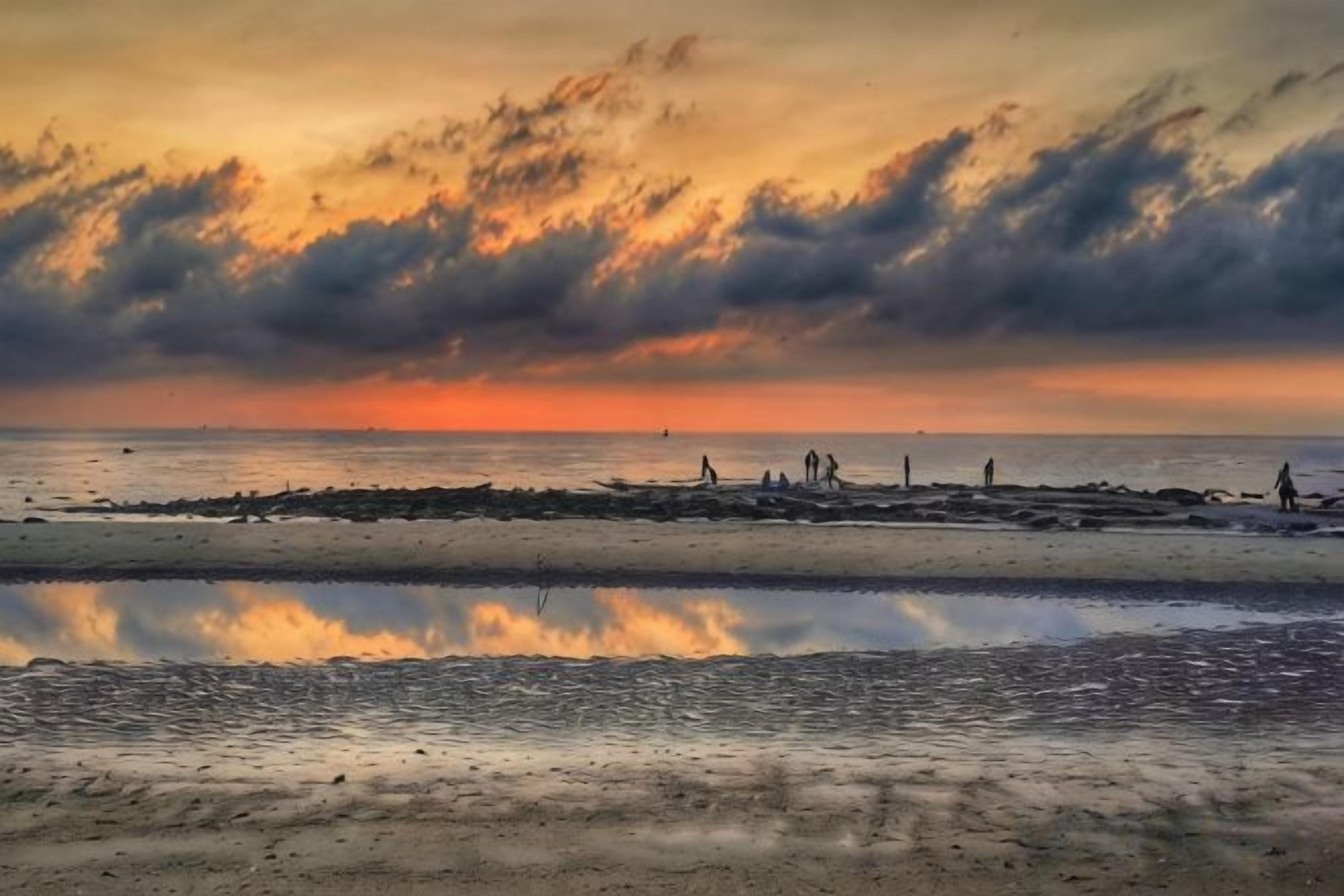 A beach with a calm sea, a reflective water surface, and a sunset in the background.