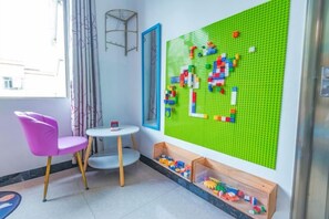 A room with a green pegboard wall, a pink chair, a small round table, and a wooden toy storage unit. - Weizhou Island Shibei Homestay (Shell Beach) (Beihai)
