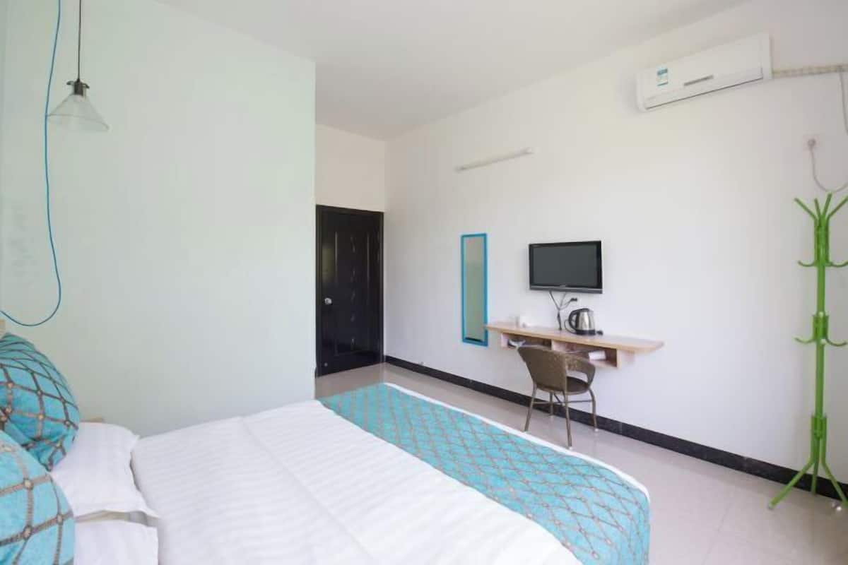 Una habitació d'hotel amb un llit, un escriptori amb un ordinador, un televisor i un aparell d'aire condicionat.