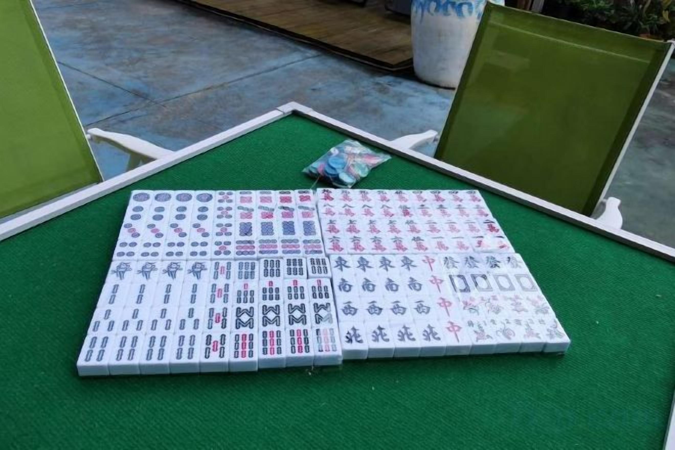 A Mahjong set with tiles arranged on a green mat, placed on a table with a white border.