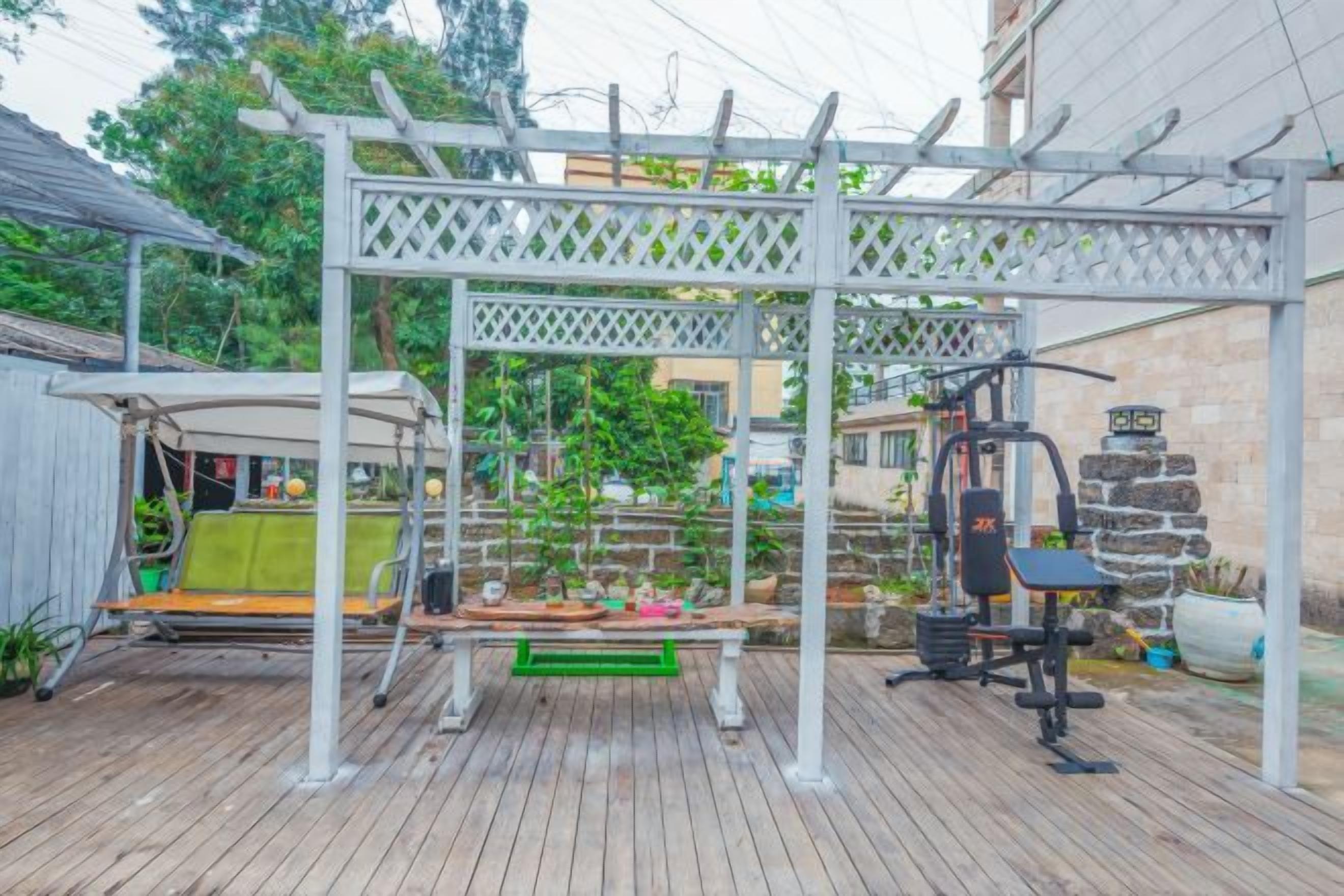 A wooden deck with a white pergola, outdoor exercise equipment, and a hanging swing.