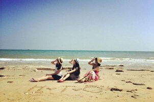 Três pessoas sentadas em uma praia arenosa, com a palavra 'LOVE' escrita na areia.