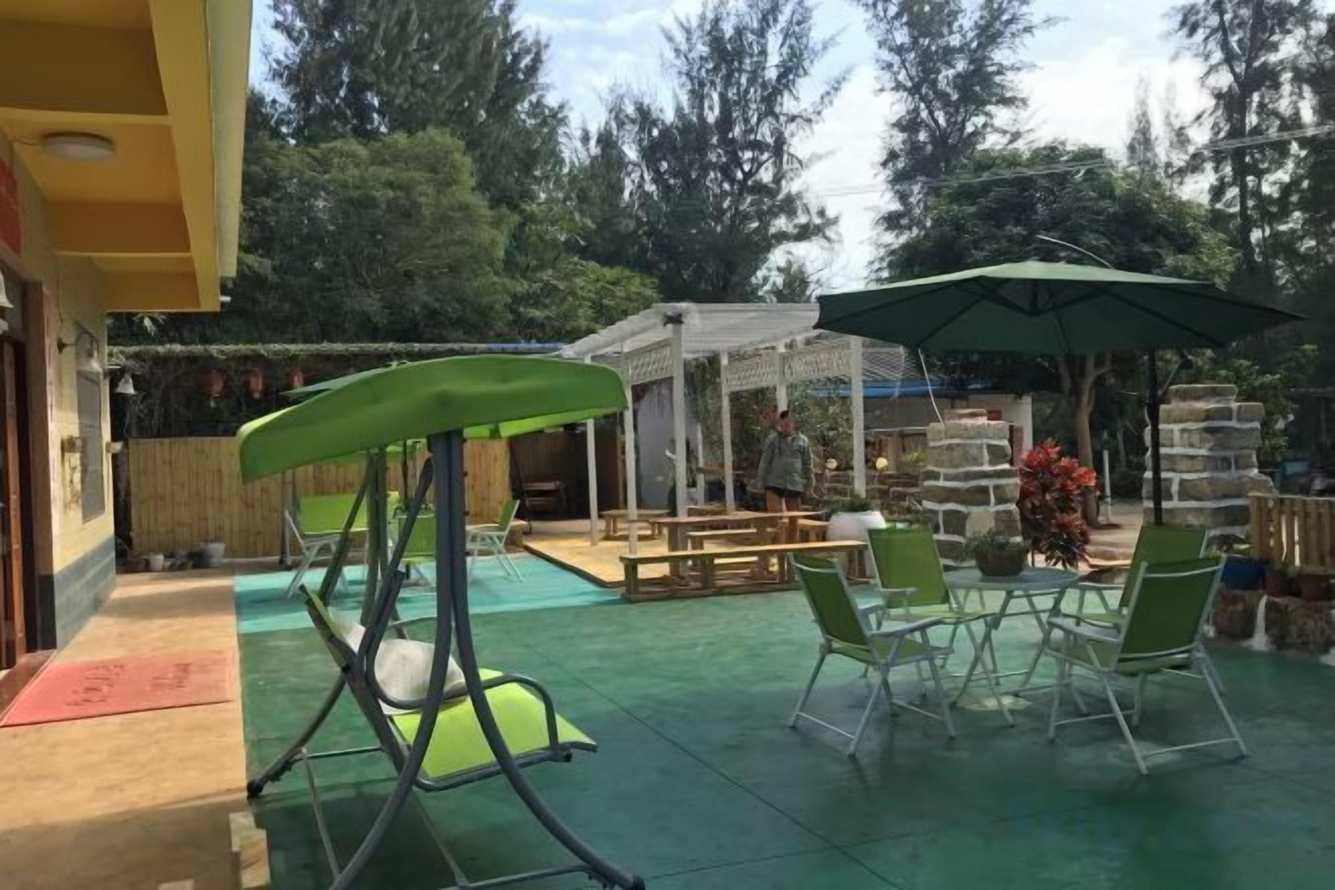 Un área de patio exterior con un columpio, sillas verdes y una zona de estar cubierta.