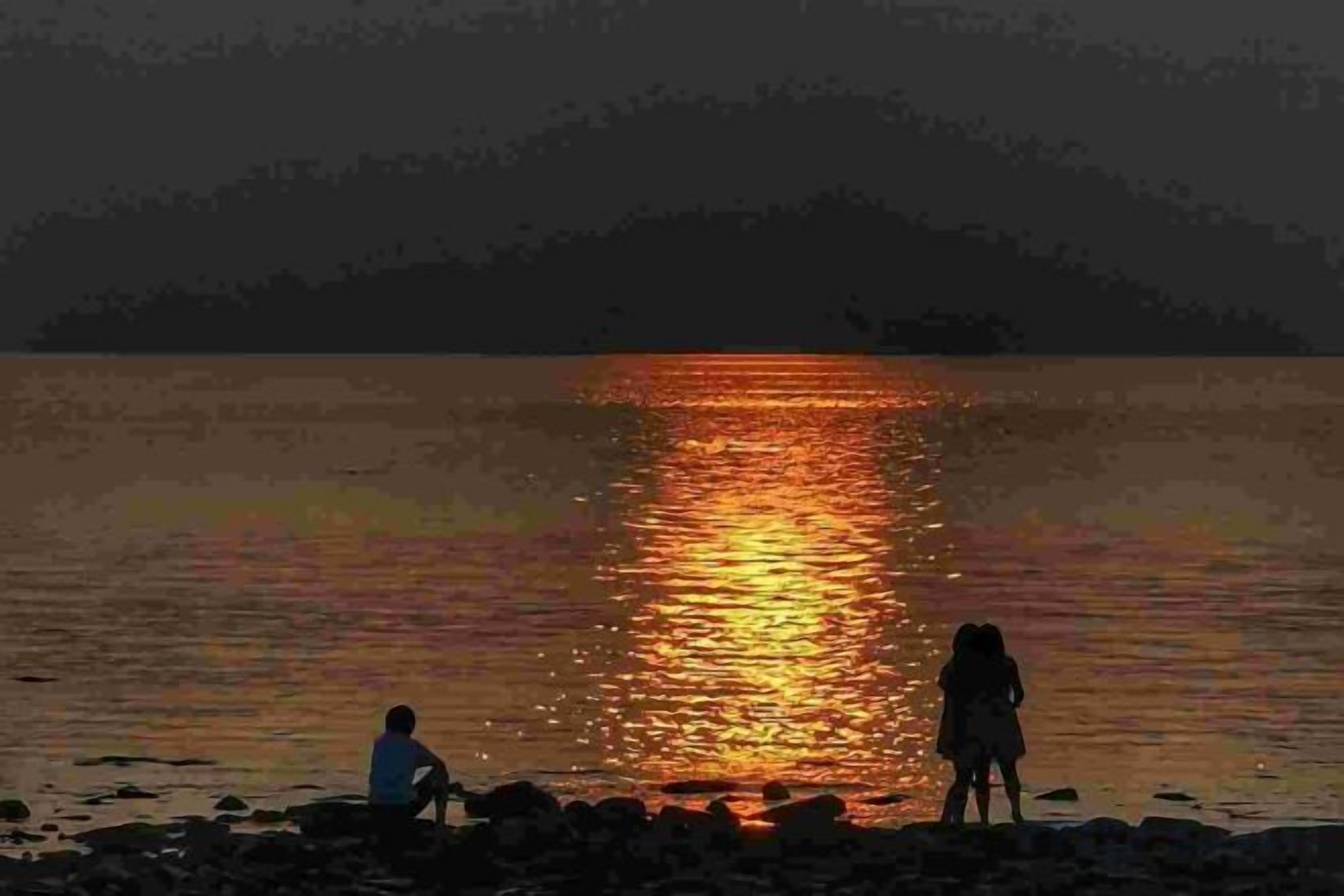 A lake with a person sitting and another standing, reflecting on the water.