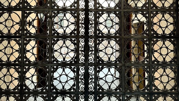 Un portail en fer forgé noir, orné de motifs complexes et doté de plusieurs fenêtres circulaires.