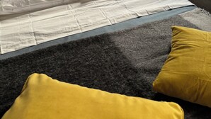 Un lit avec une literie blanche, une moquette grise et deux coussins jaunes.