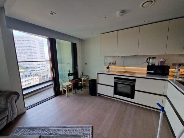 A modern kitchen with a built-in oven, microwave, and coffee maker. There is a dining area with a table and chairs, and a large window offering a city view.