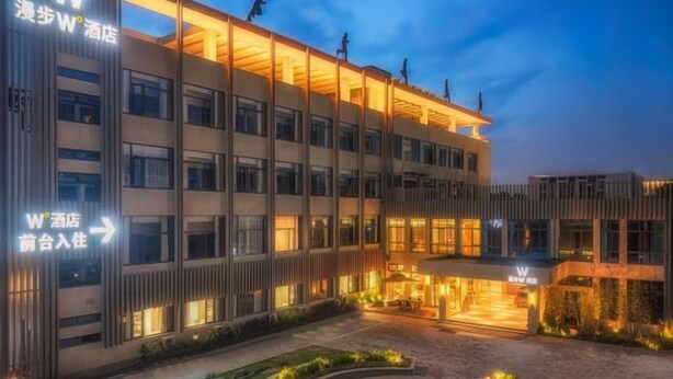 A hotel with multiple floors, a well-lit entrance, and signage indicating directions to the lobby and rooms. - Man buGarden Hotel (Ningbo)