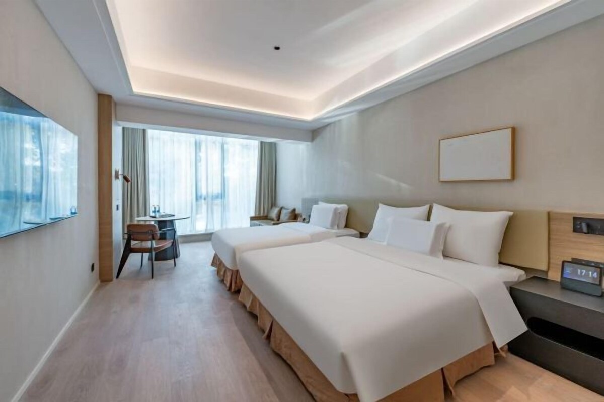 A hotel room with two beds, a desk, a chair, and a large window.