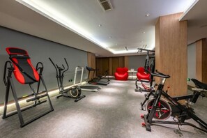 Een fitnessruimte met trainingsapparatuur, waaronder loopbanden, hometrainers en een roeimachine.