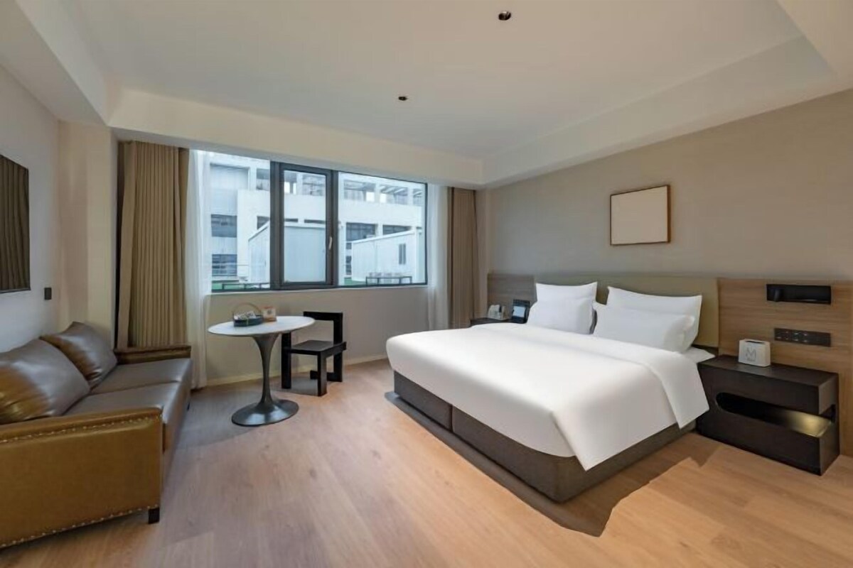 A hotel room with a bed, a sofa, a small table, and a nightstand.