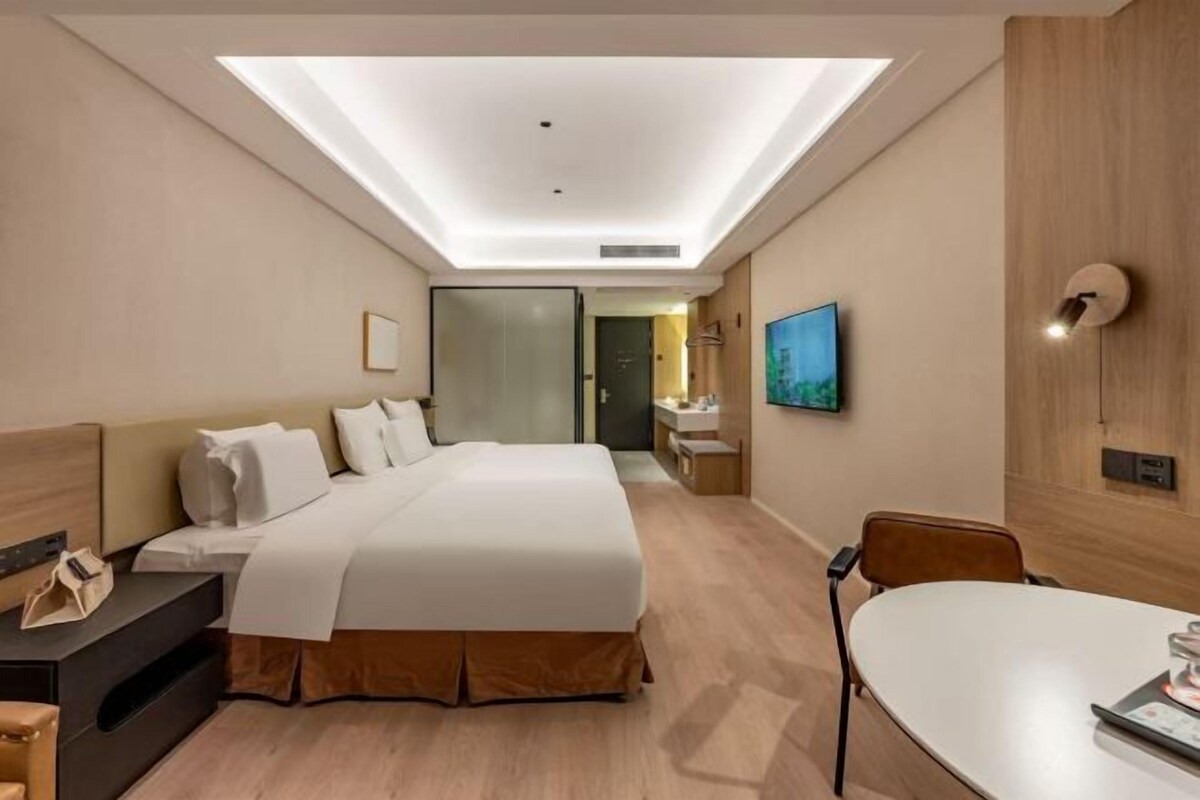 A hotel room with a large bed, bedside table, and a desk with a chair.
