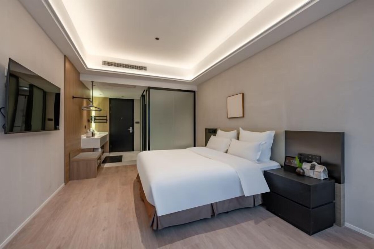 A modern hotel room with a large bed, bedside table, and a mirror.