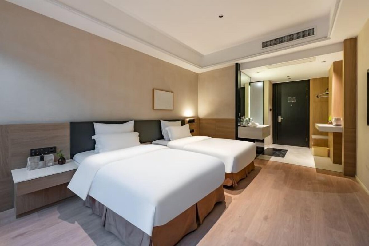 A hotel room with two beds, a bedside table, a mirror, a sink, and a shower area.