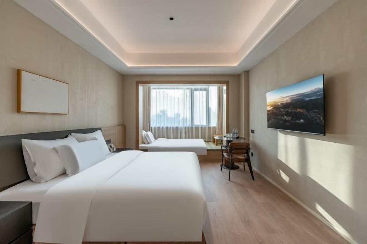 A hotel room with a large bed, a desk, a chair, and a television on the wall.