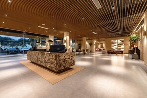 Een moderne receptie met een marmeren balie, houten plafond en uitzicht op de omgeving.