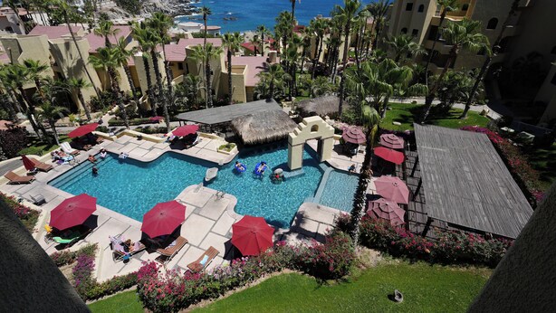 Ein Resort-Poolbereich mit mehreren Schwimmbecken, Liegestühlen, Sonnenschirmen und Palmen.