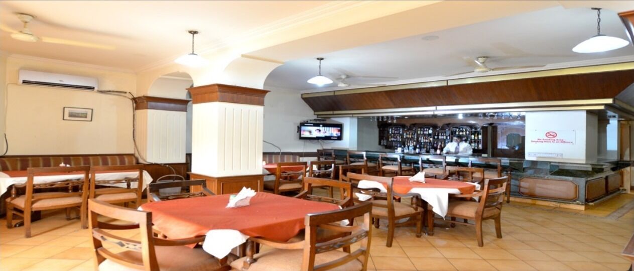 A restaurant with multiple tables and chairs, a bar area, and a television screen.