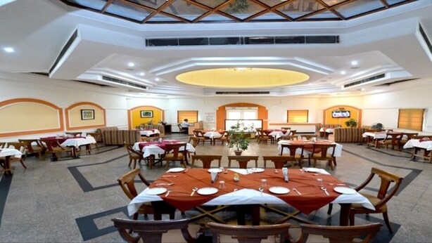 A large dining hall with multiple round tables and chairs, a central floral arrangement, and a ceiling with a skylight. - Ethnic India Tourist Resort (Sonepat)