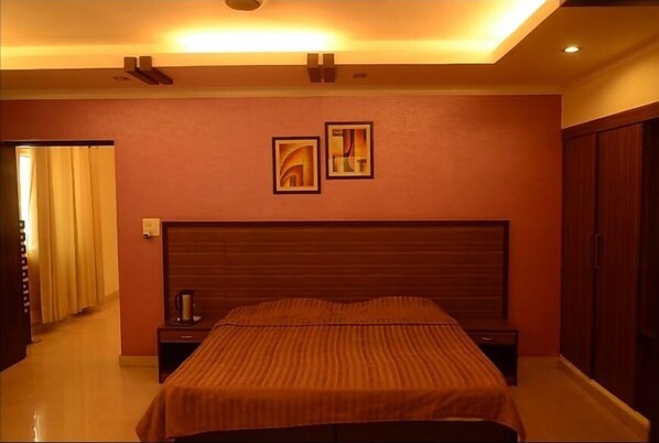 A hotel room with a large bed, a nightstand, a wall-mounted artwork, and a wardrobe. - Ethnic India Tourist Resort (Sonepat)