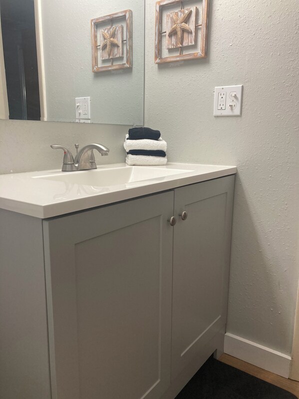 A bathroom with a white sink, two cabinets, and a mirror. There are two framed pictures on the wall above the mirror.