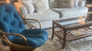 A living room with a white sofa, a blue armchair, a glass coffee table, and two lamps. - STEPS TO THE BEACH and POOL Oceanfront QUIET complex Lola’sLanding!! CouplesOnly (St. Augustine)