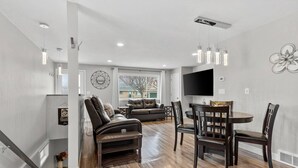 A modern living room with a sofa, chairs, and a dining table. There is a TV mounted on the wall and a window providing a view outside. - 1214 Lambeau Field Luxe (Green Bay)