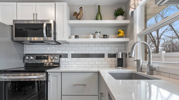 A modern kitchen with white cabinets, stainless steel appliances, a built-in oven, and a large window providing a view of the outdoors. - 1214 Lambeau Field Luxe (Green Bay)