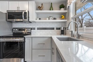 Una cocina moderna con gabinetes blancos, electrodomésticos de acero inoxidable, un horno empotrado y un amplio ventanal con vistas al exterior.