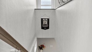 A staircase with a wooden handrail, a wall-mounted light fixture, and a decorative wall piece. - 1214 Lambeau Field Luxe (Green Bay)