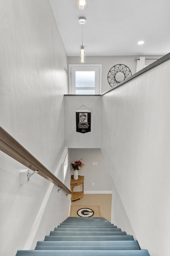 Una escalera con barandilla de madera, una lámpara de pared y un adorno en la pared.
