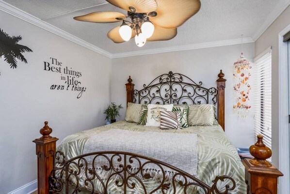 A bedroom with a bed, a ceiling fan, a wall with a quote, and a window with blinds. - Midnight Cove II Bldg 6, 2nd Fl Near Pool (Siesta Key)