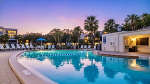 A swimming pool with lounge chairs and umbrellas, surrounded by palm trees and buildings. - Midnight Cove II Bldg 6, 2nd Fl Near Pool (Siesta Key)
