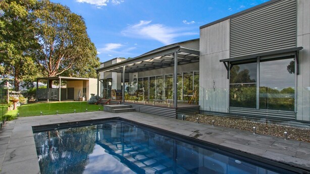 A modern house with a swimming pool, large windows, and a covered outdoor area.